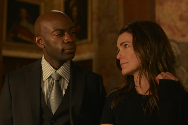 David Gyasi in a suit and Keri Russell all in black, gazing at each other.
