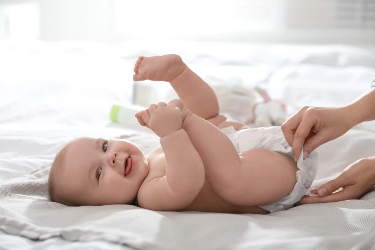 A person changing a baby's diaper on a bed.