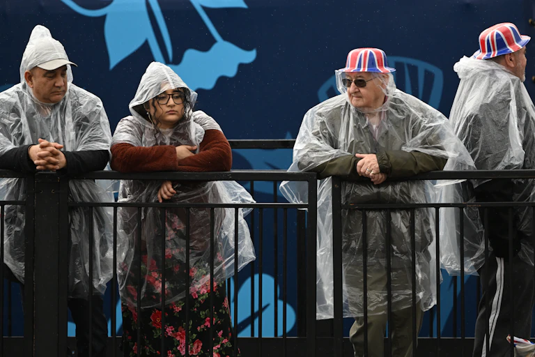 Four people in transparent ponchos rest against a railing.