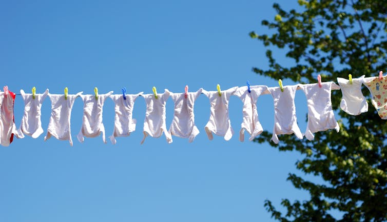Clothes line full of reusable baby diapers in front of a clear blue sky.
