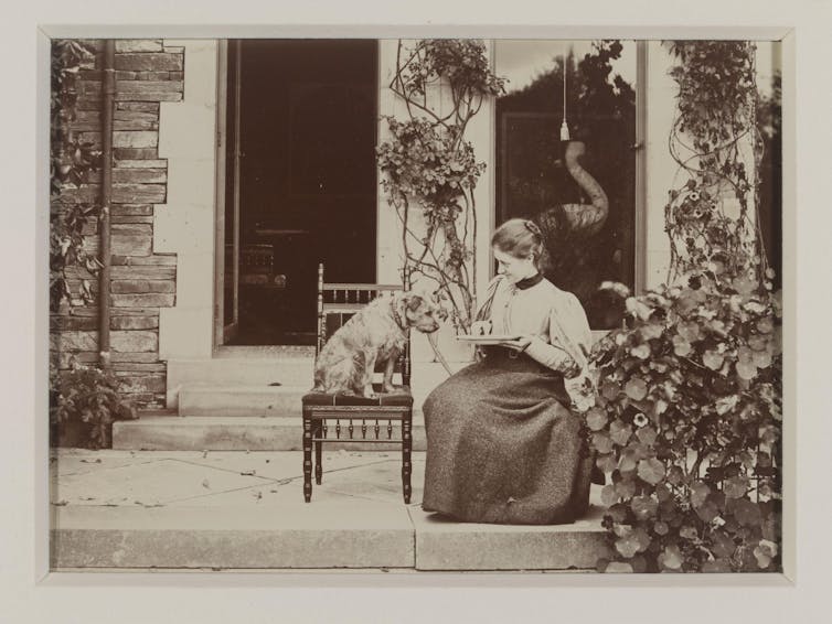 A black and white photo of a woman sitting with a dog outside a house.