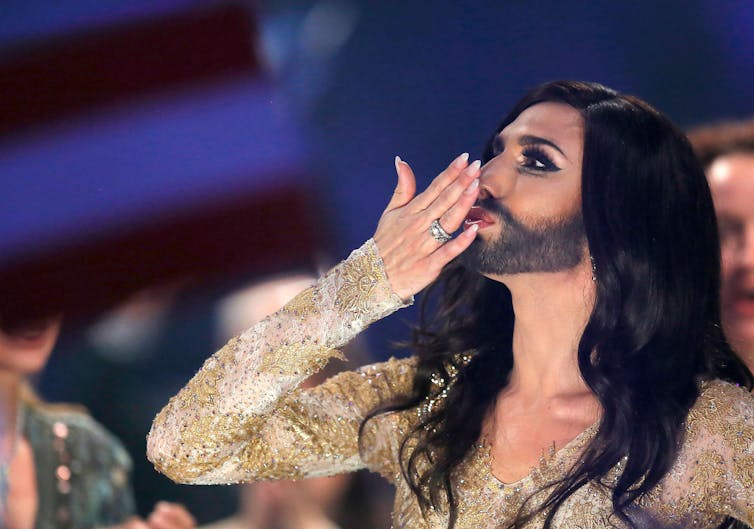 Beareded drag queen Conchita Wurst blowing a kiss on stage