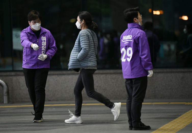 Two women in purple jackets hand out stickers.