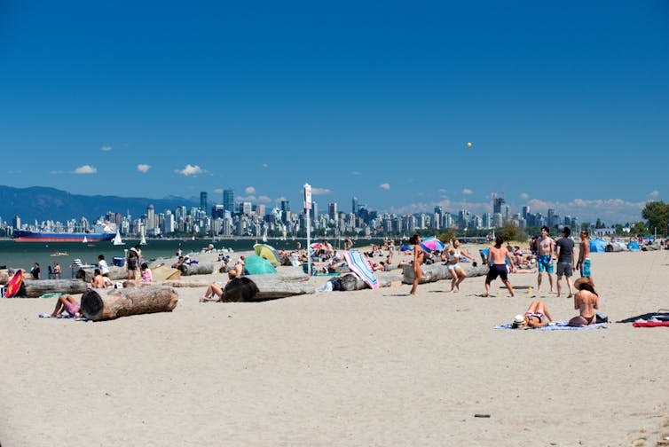 People at a beach. A city skyline is visible in the background.