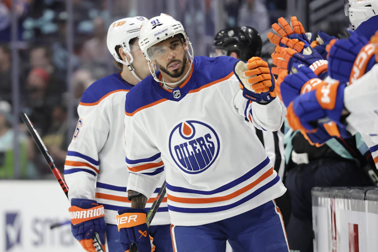 A Black man in a hockey uniform bumps the fists of his teammates as he skates along the bench.