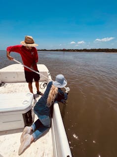 Two people on a boat collecting water samples from a river