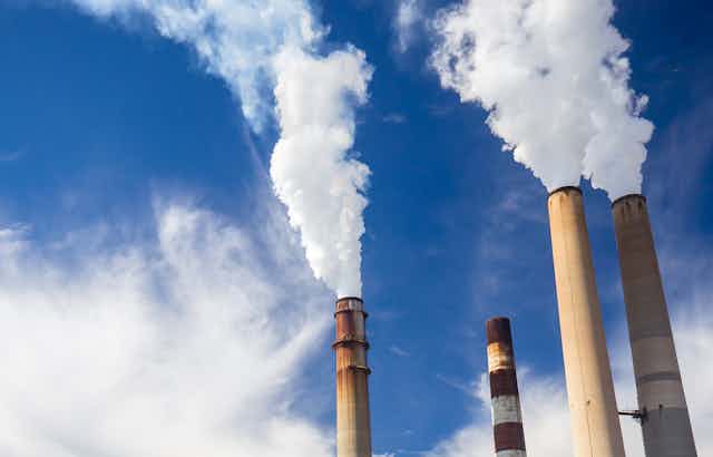 A power plant with a blue sky with clouds behind it and four smokestacks