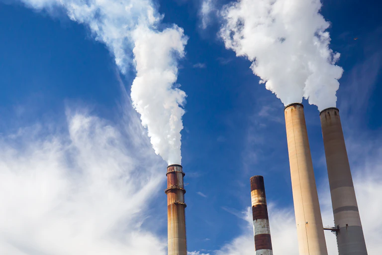 A power plant with a blue sky with clouds behind it and four smokestacks