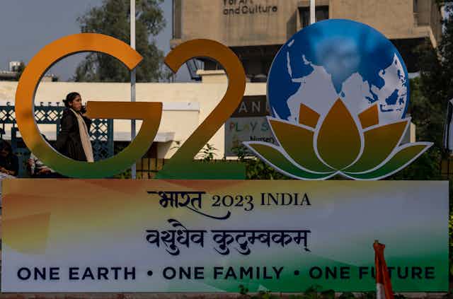 A woman on a cellphone walks past a yellow and green display that says: G20 2023 India One earth one family one future