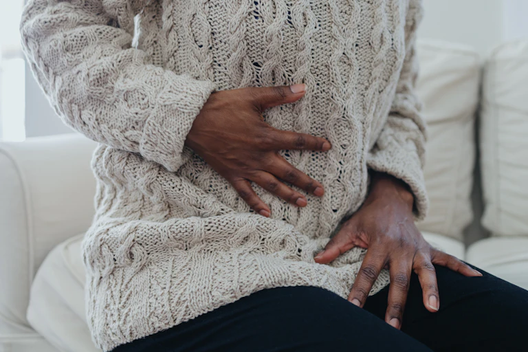 A hand clutching at the stomach as if in pain while the other grips the thigh.