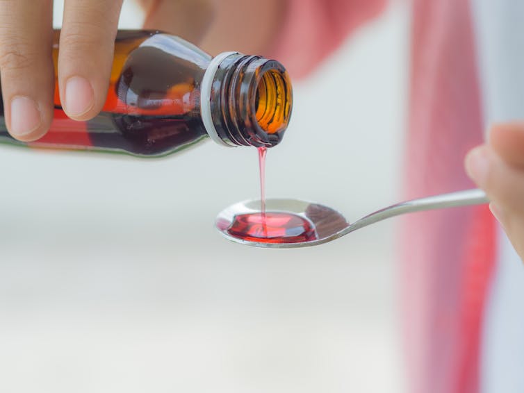 Person pours cough syrup onto a spoon