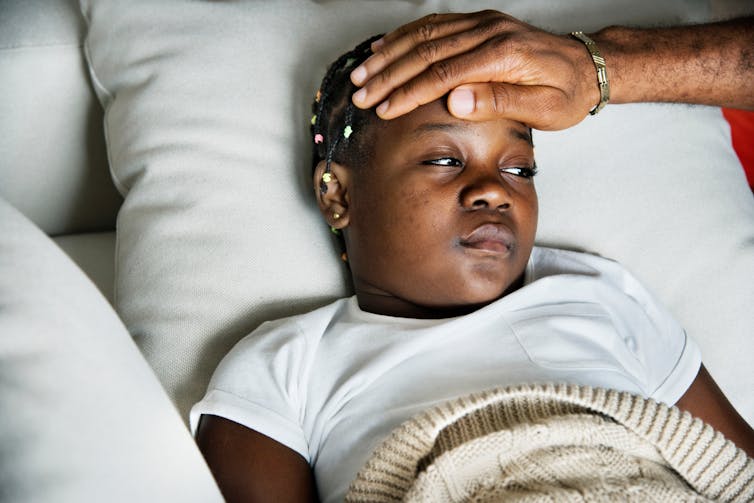 Girl with a fever looks at her Dad, whose arm is touching her head