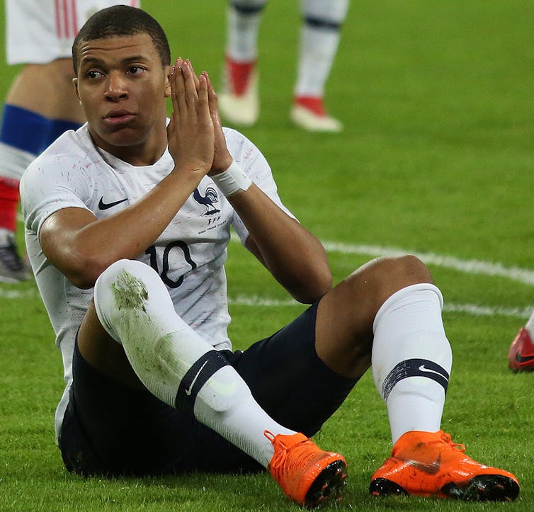 Kylan Mbappé assis sur un terrain de foot, ici en 2018