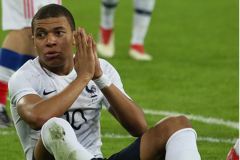 Kylan Mbappé assis sur un terrain de foot, ici en 2018.