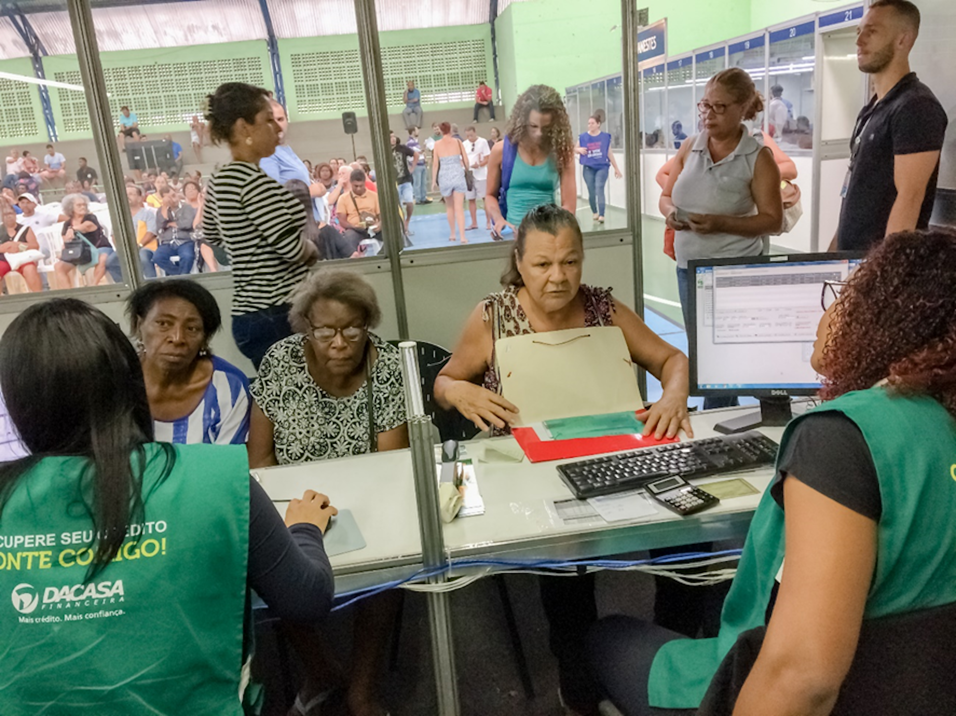 Renégociation de dettes entre débitrices (pour la plupart des femmes racisées et âgées) et agentes de recouvrement (en vert et de dos). Décembre 2019, foire de renégociation des dettes de Vitoria (Espirito Santo) Brésil
