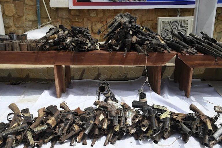 Plusieurs armes saisies sont exposées sur le sol et sur des tables.