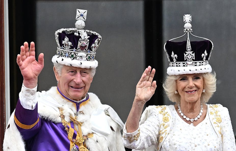 A man and woman wearing diamond crowns wave to crowds.