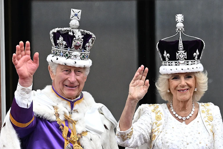 A man and woman wearing diamond crowns wave to crowds.