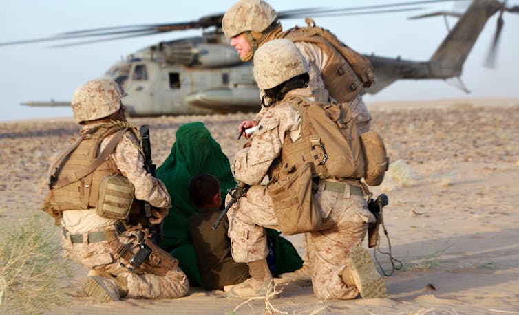 Female soldiers talking to a local woman in front of a helicopter