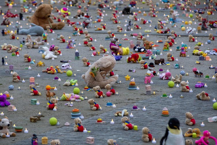 Rows of teddy bears are spread out across the ground, with small fake candles nearby.