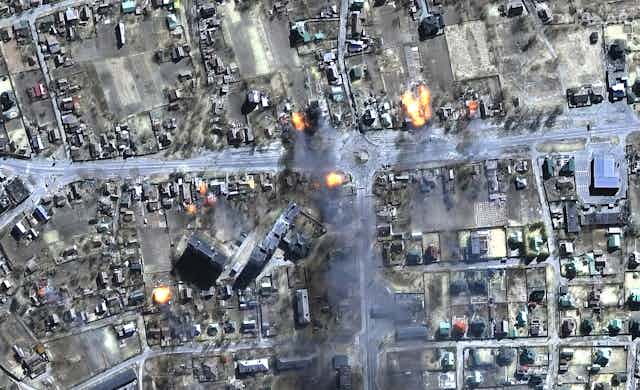 A satellite image shows rows of houses and road and a few fires breaking out.
