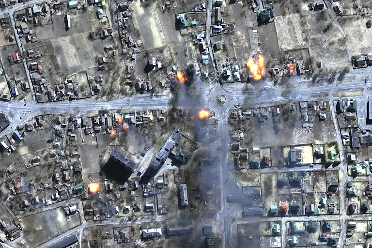 A satellite image shows rows of houses and road and a few fires breaking out.