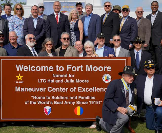 A group of people are standing near a sign that welcomes visitors to Fort Moore.