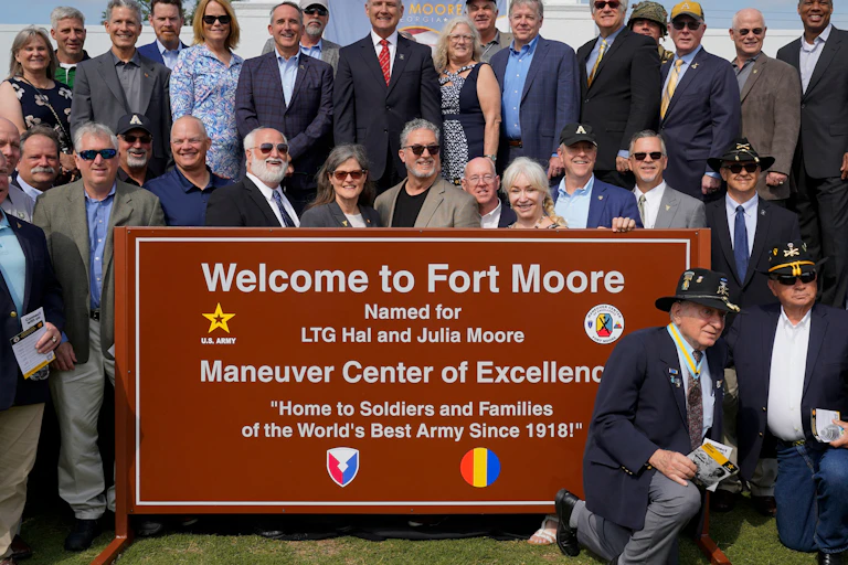 A group of people are standing near a sign that welcomes visitors to Fort Moore.