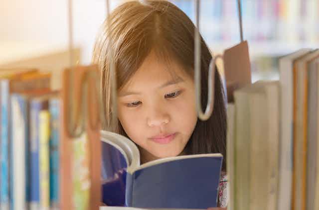 A young girl reads a book in a library.