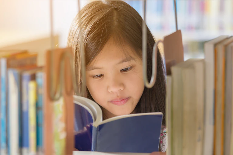 A young girl reads a book in a library.