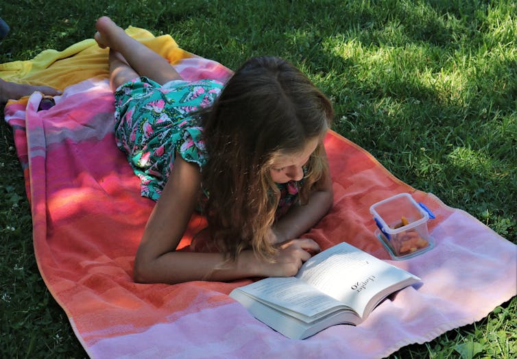 A young girls reads on a towel on the grass.