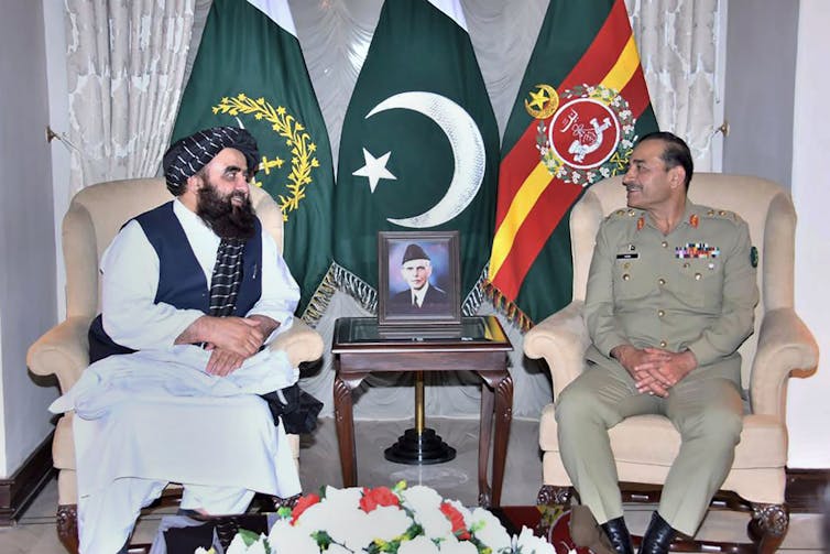 picture of a military officer sitting next to a man wearing traditional cloths
