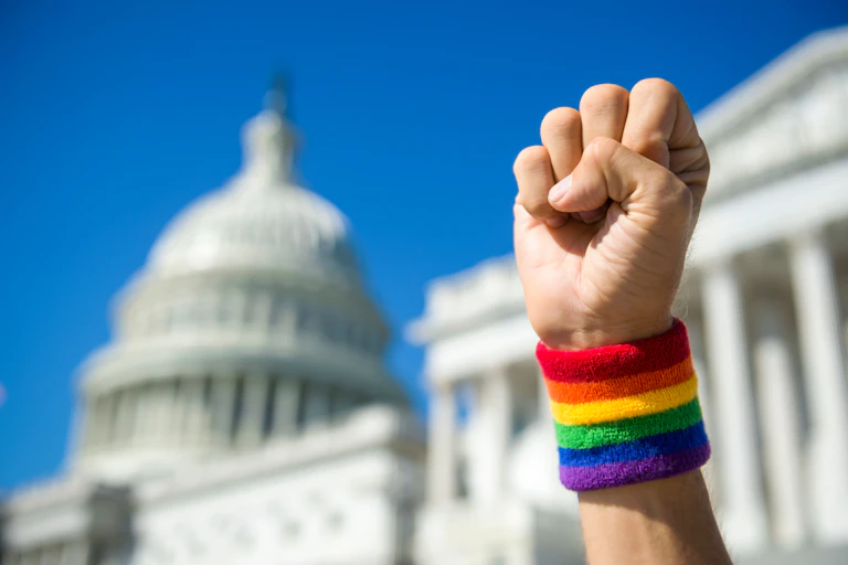 Bras tendu avec un bracelet aux couleurs de l'arc-en-ciel, le poing levé