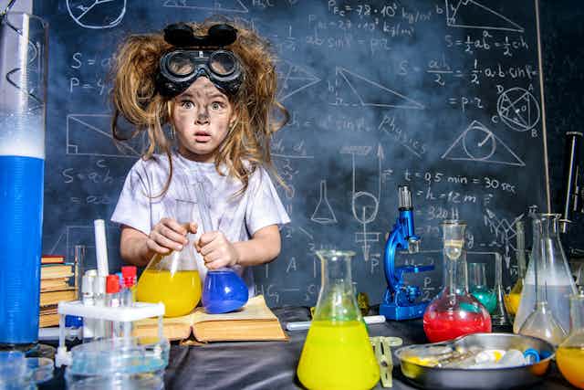 Una niña con pelos locos haciendo experimentos químicos ante una pizarra llena de fórmulas.
