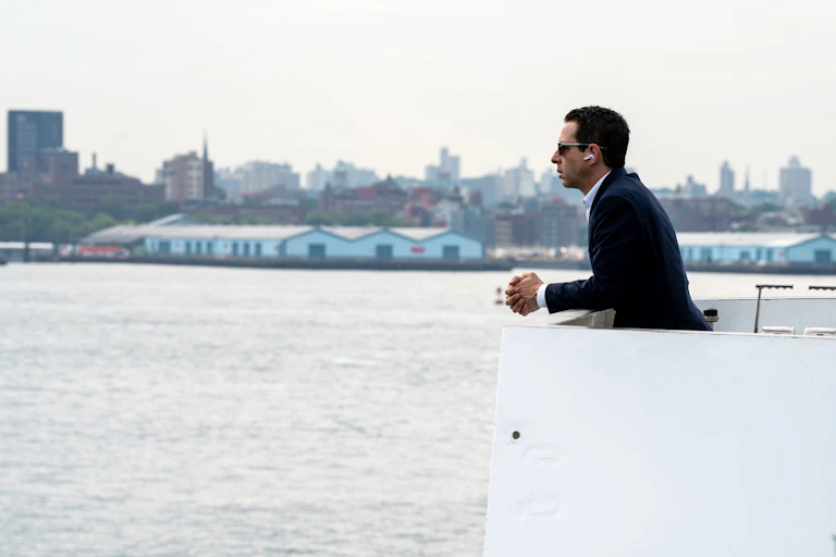 Kendall Roy wearing AirPods on a boat, in a black suit.