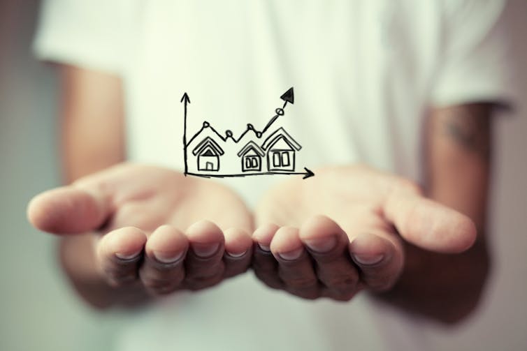 Hands cupped underneath chart showing rising house values.