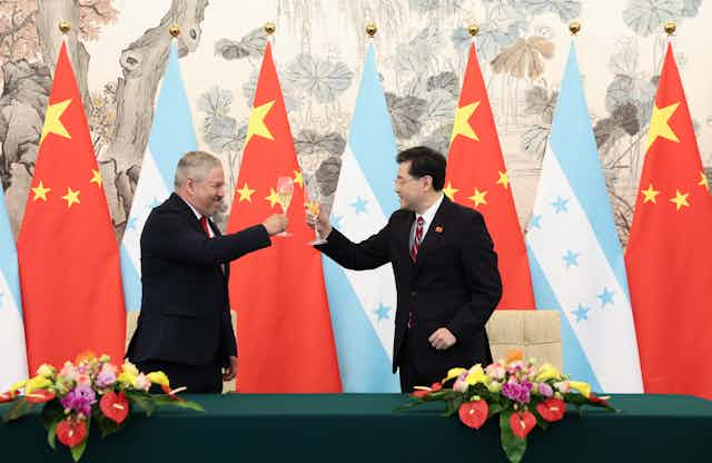 wo men toast each other with champagne glasses in front of Chinese and Honduran flags.