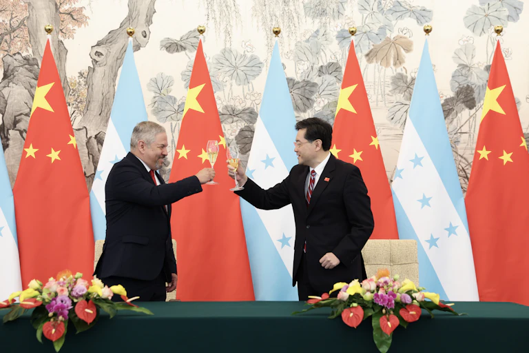 wo men toast each other with champagne glasses in front of Chinese and Honduran flags.