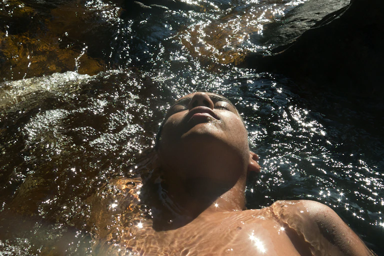 Teen lying in river as water washes over him.