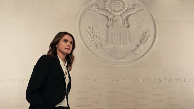 Una mujer con traje delante del escudo de Estados Unidos de América.