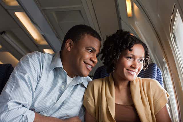 Man and woman sit close together and smile as look out airplane window
