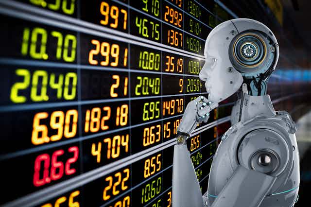 a gray robot strokes his robot chin with left robot hand while staring at a screen of numbers that resemble stock prices