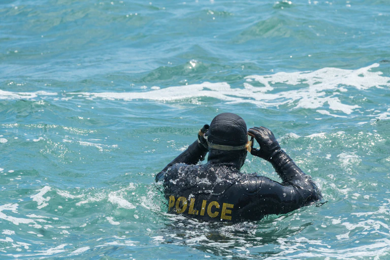 A diver in a wet suit that says police on the back standing in choppy sea water