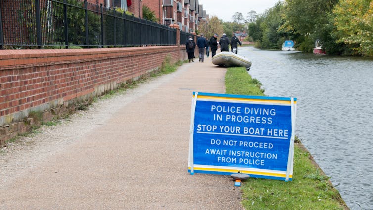 A sign on the side of a footpath that says police diving is underway and people should stop their boats before proceeding