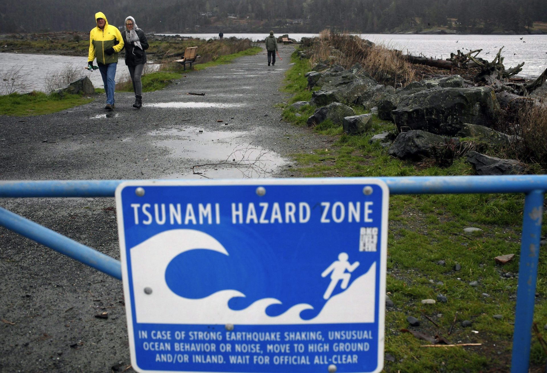A couple walks along a tsunami warning sign