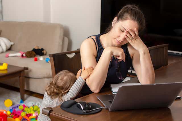 tired mother at desk with small child tugging on her arm