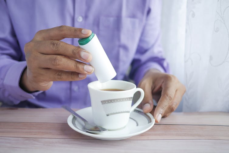 person puts sweetener in cup of tea