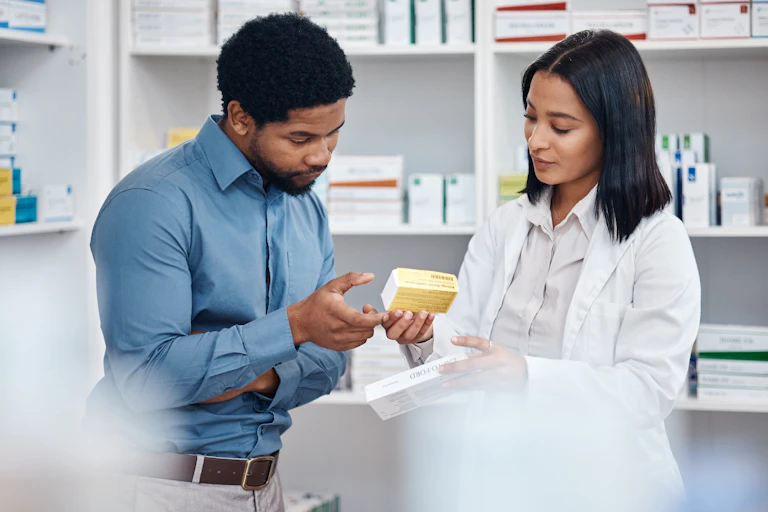 A young man looks at the medicine box his female pharmacist is holding.