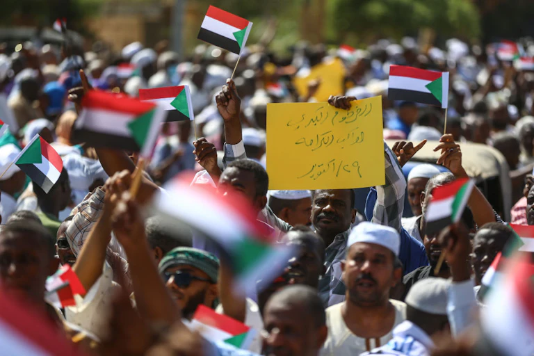 A crowd of people walking while holding up small red, white, black and green flags
