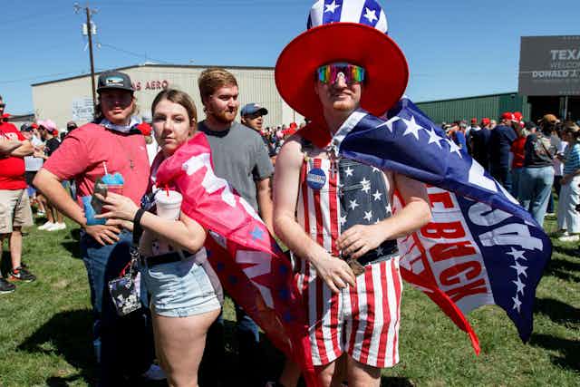 Two Donald Trump supporters wearing flags, one with a hat, looking towards the camera.